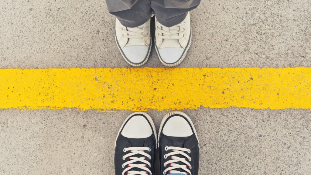 This image shows two sets of feet in trainers from above, standing at dividing line. - Feeling out of control